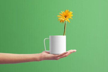 hand holding a white cup.Orange flower in the cup. White cuo on the green background.