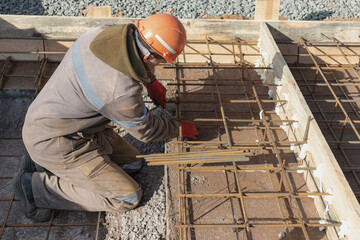 A worker uses steel tying wire to fasten steel rods to reinforcement bars. Reinforced concrete...