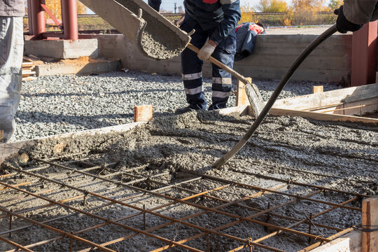 Pouring cement or concrete with a concrete mixer truck, construction site with a reinforced grillage foundation. Workers settle and level the concrete in the foundation.