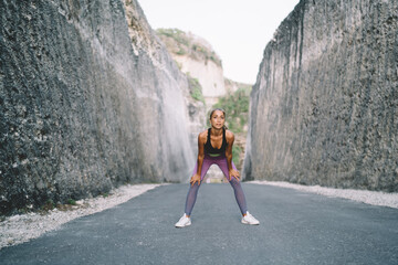 Caucasian female in tracksuit stretching during morning workout training for reaching vitality during sportive practice, slim motivated woman keeping healthy lifestyle doing exercise outdoors