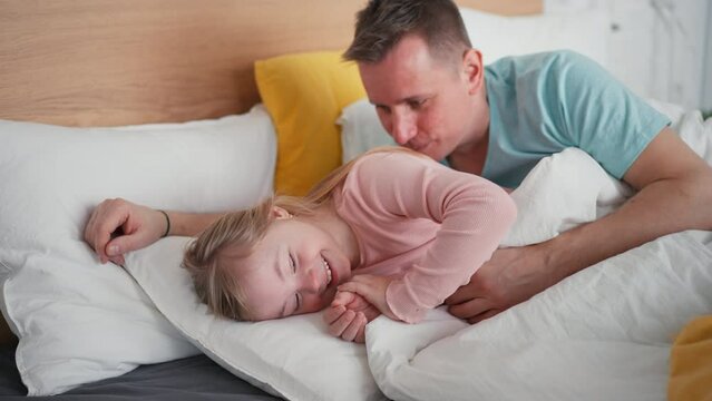 Father resting with his little daughter with Down syndrome in bed at home.