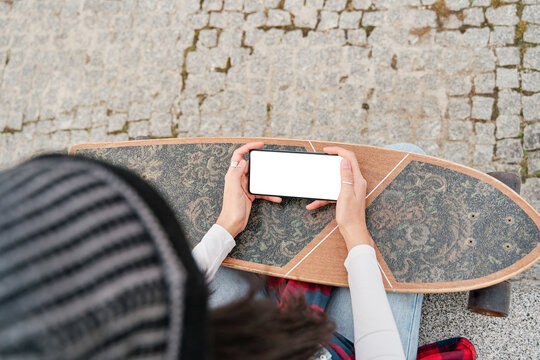close-up of the hand holding the blank screen of the mobile phone. view of a woman with a skateboard. - Powered by Adobe