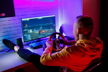 Male gamer playing racing games on the computer. He uses the steering wheel. Emotional game © DSMT