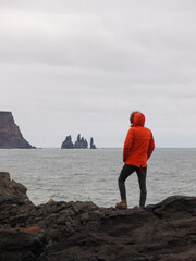 Iceland landscape photo of man in a red jacket in front of Reynisfjara black-sand beach found on the South Coast of Iceland.