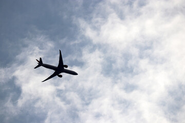 Silhouette of airplane flying in the cloudy sky, bottom view. Commercial plane, international air traffic