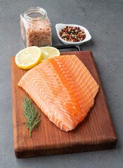 Raw salmon fillet with seasonings over wooden board