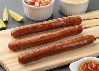 Pork sausage skewers over wooden board with farofa, lemon and vinaigrette