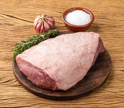 Raw picanha or rump meat over wooden board with seasonings