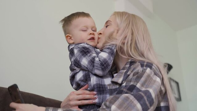 Young Mom With A Little Child In The Same Sweatshirts, Taking A Selfie, The Child Hugging