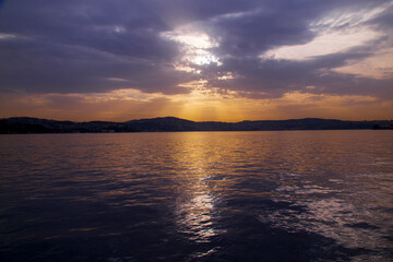 amazing colorful clouds on sunset. Beautiful golden sunset in the sea with saturated sky and clouds. Reflection in the water. Rocky coastal line. Peaceful serene landscape. Nature background.