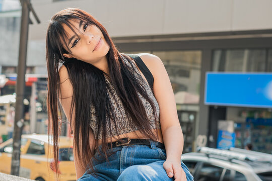 beautiful latin woman with brown skin, sitting on the sidewalk in the streets of the city of Pereira-Colombia. student girl with face and tender look looking at the camera. concept of love.