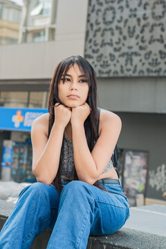 beautiful latin woman with brown skin, sitting on the sidewalk in the streets of the city of Pereira-Colombia. university girl sitting on the street with her hands on her face. love disillusionment