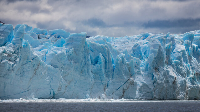 Eine Mauer aus massiven Eis und spitzen Eiszacken ragt empor. Das Eis des Perito Moreno Gletschers in Patagonien erstrahlt in einem glazialen Blau und beeindruckt seine Besucher durch die Größe