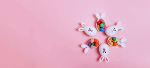 Top view Easter pink background with flower shape made of funny eggs containers with bunny ears...