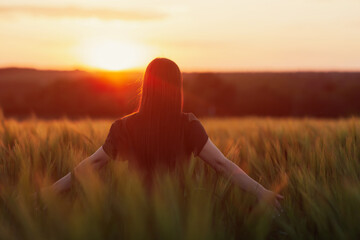 Freedom girl enjoying nature in wheat field. Beautiful girl in green dress walking on the field at sunset light.