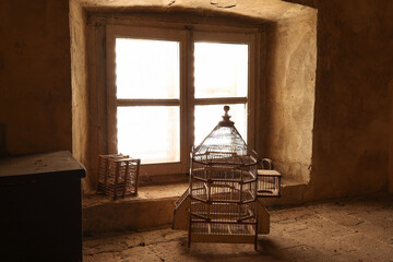 two empty old wooden bird cages in a attic in front of a window