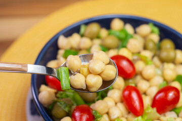 spoon with chickpeas with leaves, olives and tomatoes in a blue bowl