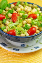 superclose of spoon with chickpeas with leaves, olives and tomatoes in a blue bowl on the table