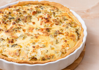 Sliced traditional French open quiche pie with feta cheese and scallion on a light brown...