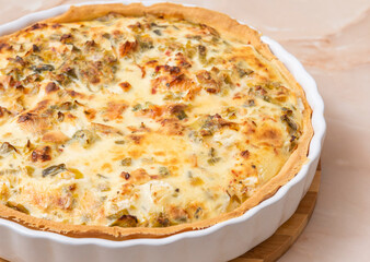 Sliced traditional French open quiche pie with feta cheese and scallion on a light brown background. Image from an angle.