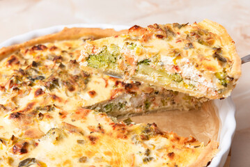 Sliced traditional French open quiche pie with feta cheese and scallion on a light brown...