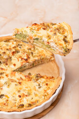 Sliced traditional French open quiche pie with feta cheese and scallion on a light brown background. Image from an angle.