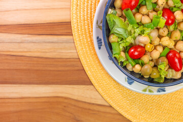 top view of chickpeas with leaves, olives and tomatoes in a blue bowl on the table