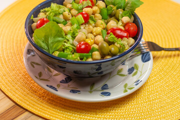 spoon with chickpeas with leaves, olives and tomatoes in a blue bowl on the table