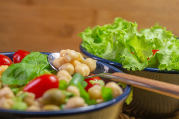 spoon with chickpeas with leaves, olives and tomatoes in two bowls on the table