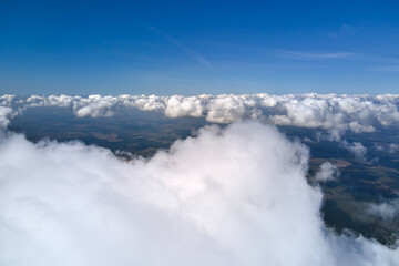 Aerial view from airplane window at high altitude of earth covered with white puffy cumulus clouds