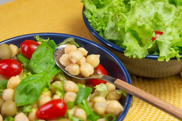 spoon with chickpeas with leaves, olives and tomatoes in two bowls on the table