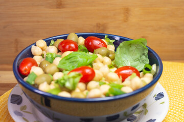 spoon with chickpeas with leaves, olives and tomatoes in a blue bowl on the table