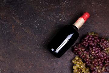 Ripe sweet grapes, wine bottle  on dark background. Flat lay, top view image with copy space.