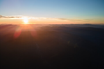 Aerial view of dark mountain hills with bright sunrays of setting sun at sunset. Hazy peaks and misty valleys in evening