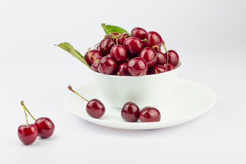 Ripe sweet cherries in a white bowl and on plate on white background.