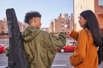back view portrait of youngster salutating each other with bumping fists. latin teenager with a...