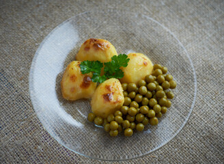 Baked potatoes with peas on a transparent glass plate