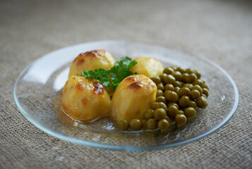 Baked potatoes with peas on a transparent glass plate