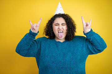 Young beautiful woman wearing a birthday hat over isolated yellow background shouting with crazy...