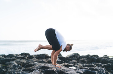Caucasian man in casual sportswear doing asana poses for recreating during time for feeling mindfulness and appeasement, flexible male healing during holistic retreat training at coastline