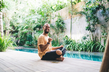 Portrait of excited man freelancer celebrate achievement of successful online project and approved deal, overjoyed male with laptop computer feeling accomplished with digital nomad at pool terrace