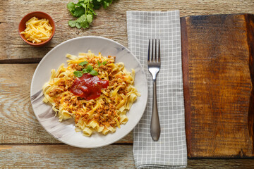 Pasta bolognese garnished with herbs and cheese in a plate on a wooden table on a stand next to a fork and a napkin.
