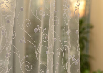 White light tulle on the window against the background of the sunset. White tulle with pattern