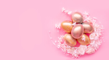 Obraz na płótnie Canvas Golden eggs in a flower nest on a pink background . Easter concept with space for text