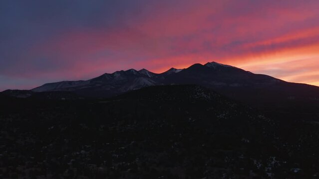 A purple and red sunset sky behind Humphreys Peak and the Kachina Peaks, north of Flagstaff, Arizona. An aerial dolly out shot.