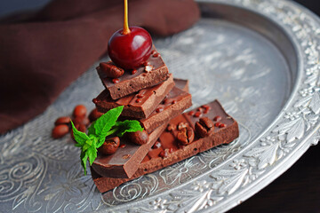 Pieces of chocolate, cherries and a sprig of mint on a silver tray.