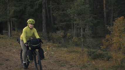 Obraz premium The woman travel on mixed terrain cycle touring with bike bikepacking outdoor. The traveler journey with bicycle bags. Stylish bikepacking, bike, sportswear in green black colors. Magic forest park.