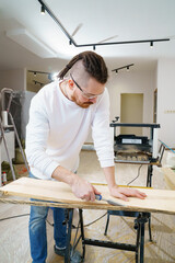 carpenter in protective gloves and glasses cuts bark from wood with chisel