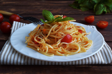Spaghetti pasta with tomatoes and basil on a wooden table.