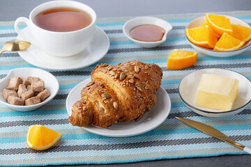 Fresh croissant with butter and tea, orange for breakfast